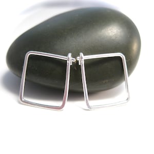 May include: A pair of silver square hoop earrings. The earrings are simple and modern in design.