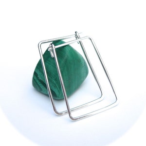 May include: A pair of silver square hoop earrings. The earrings are made of a thick, polished metal and have a simple, modern design.