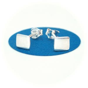 May include: A pair of silver square stud earrings. The earrings are small and simple, with a brushed finish.