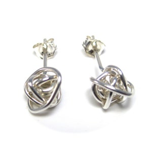 May include: A pair of silver knot earrings. The earrings are made from a single piece of wire that is twisted and knotted into a ball shape. The earrings are simple and elegant.