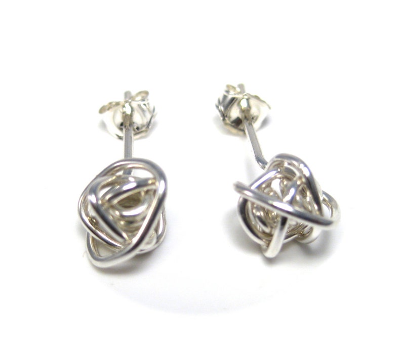 May include: A pair of silver knot earrings. The earrings are made from a single piece of wire that is twisted and knotted into a ball shape. The earrings are simple and elegant.