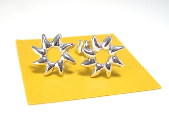 May include: A pair of silver star-shaped earrings with a textured surface. The earrings are on a yellow background.