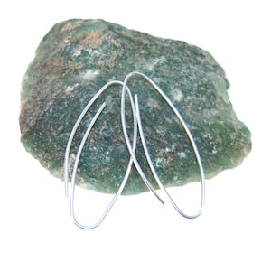 May include: A pair of silver oval hoop earrings on a green rock background.