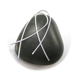 May include: A pair of silver wire earrings with a simple, modern design. The earrings are shown on a dark gray stone.