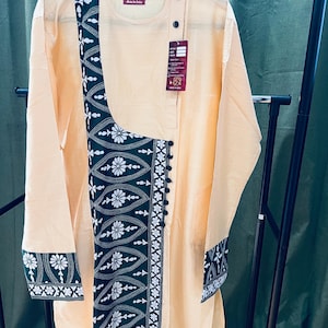 May include: A light beige long-sleeved shirt with a green and white embroidered design on the front and sleeves. The shirt has a button closure at the neck and a side slit.