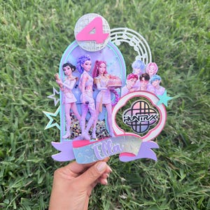 May include: A multi-layered cake topper featuring a large pink number 4, a disco ball graphic, and illustrations of pop music characters. The design includes a circular logo with the text HUNTRX and a banner at the bottom with the name Ella.