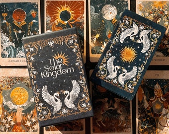 Może przedstawiać: Pudełko kart tarota The Solar Kingdom z czarnym tłem i złotymi napisami. Pudełko jest otwarte i pokazuje karty w środku, które przedstawiają ilustracje łabędzi, gwiazd i księżyców. Karty są ułożone w siatkę na jasnobrązowej powierzchni.
