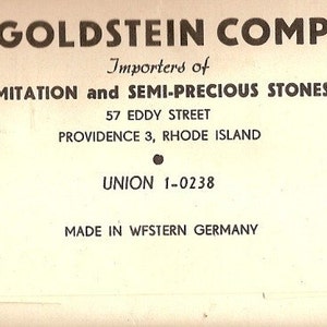 May include: Black and white business card for E. W. Goldstein Company, importers of imitation and semi-precious stones. The card lists the company's address as 57 Eddy Street, Providence 3, Rhode Island, and phone number as Union 1-0238. The card also states "Made in Western Germany."