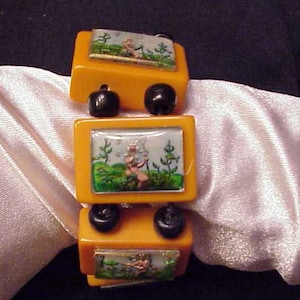May include: A vintage bracelet made of three orange plastic sections with black beads. Each section features a small, rectangular picture of a fairy in a field.