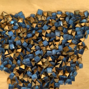 May include: A pile of blue and gold pyramid-shaped studs. The studs are made of metal and have a shiny finish.