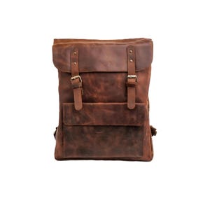Könnte beinhalten: Ein brauner Lederrucksack mit Klappenverschluss und zwei Schnallenriemen. Der Rucksack hat eine Vordertasche und verstellbare Schultergurte. Das Leder hat einen Used-Look.