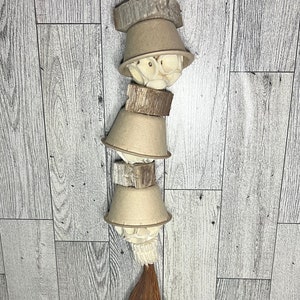 May include: A hanging bird toy made of natural materials. It features stacked beige cups, wooden blocks, and a coconut husk base, all suspended by a natural fiber cord. The toy is designed to provide enrichment for pet birds.