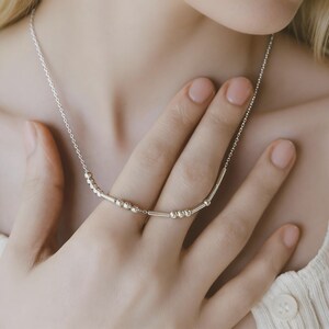 May include: A delicate silver necklace with small, round beads and slender bar-shaped elements. The necklace is shown against a soft background, highlighting its minimalist design and subtle shine. The necklace is approximately 40 cm long.