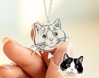 May include: A silver necklace with a pendant featuring a black and white line drawing of a cat's face. The pendant is shaped like the cat's head.