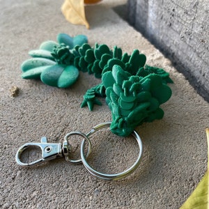 May include: A green 3D printed dragon keychain with a silver split ring and a silver lobster clasp.