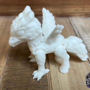 May include: A white, articulated griffin figurine with a bird-like head, feathered wings, and a horse-like body. The griffin is posed on a wooden surface, showcasing its detailed design. The figurine is a fantasy creature.