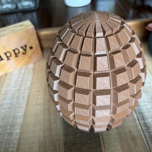 May include: A brown chocolate egg shaped like a sphere with a geometric pattern. The egg is made of many small squares that are arranged in a grid pattern.