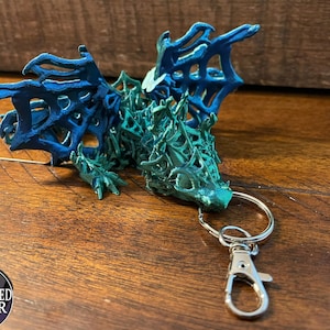 May include: A green and blue 3D printed dragon keychain with a silver metal key ring and clasp.
