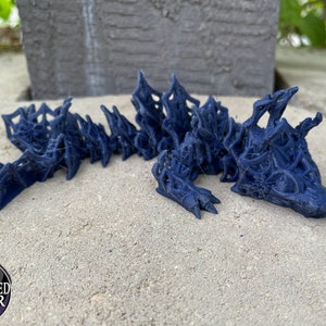 May include: A dark blue 3D printed dragon sculpture with a detailed, intricate design. The dragon is lying on its belly with its head turned to the side.