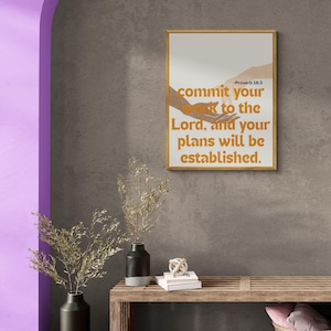 Könnte beinhalten: Ein rechteckiger Wandkunstdruck in einem dünnen Holzrahmen mit zwei ausgestreckten Händen und dem Text: commit your work to the Lord, and your plans will be established. -Proverb 16:3. Der Text ist in fetter orangefarbener Schrift auf hellem Grund.