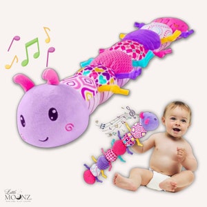 Puede incluir: Un juguete de oruga colorido y multitexturado con una cabeza morada y un diseño de nota musical. El juguete está hecho de tela suave y tiene una variedad de texturas para que los bebés exploren. El juguete se muestra con un bebé jugando con él.