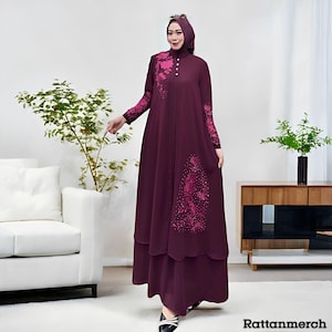 May include: A long, flowing burgundy dress with floral accents in a darker shade of pink. The dress features long sleeves and a high neckline with button details. The model is wearing a matching head covering. The text "Rattanmerch" is visible at the bottom right.