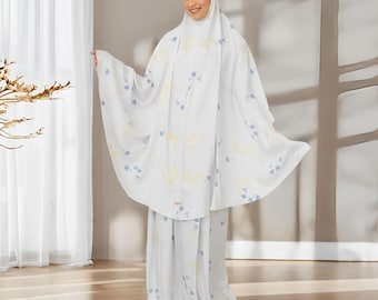 May include: White prayer outfit with a floral pattern in blue and yellow. The outfit includes a long skirt and a matching top with a hood.