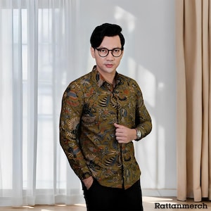 May include: A man wearing a green and brown patterned long-sleeve shirt with a button-down collar. He is wearing black pants and black-framed glasses.