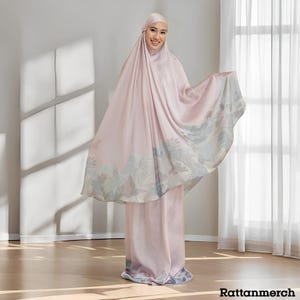 May include: A light pink prayer garment and matching head covering. The garment has a landscape design in shades of blue, grey, and green along the hem. The fabric appears to be a soft, flowing material.