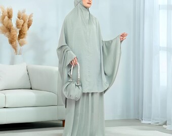 May include: A light green prayer outfit, including a head covering, long dress, and matching purse. The outfit has a flowing design and is made of a soft, silky material. The purse has a pearl handle. The text "Rattanmerch" is visible at the bottom.