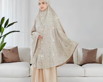 May include: A beige prayer garment with a floral pattern. The garment includes a head covering and a long, flowing robe. The bottom portion is a solid, light beige color. The text "Rattanmerch" is visible at the bottom right.