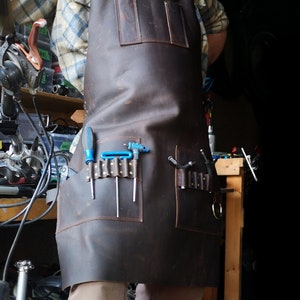 May include: A brown leather apron with multiple pockets and tool loops. The apron has a blue screwdriver and several Allen wrenches in the pockets.