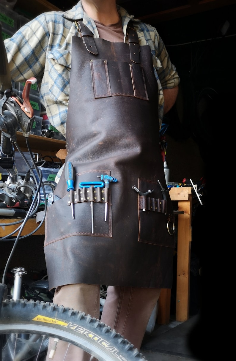 May include: A brown leather apron with multiple pockets and tool loops. The apron has a blue screwdriver and several Allen wrenches in the pockets.