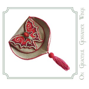 May include: A small, beige, beaded purse with a red beaded butterfly design and a red tassel. The purse is closed and the butterfly design is on the front. The text "On Graceful Gossamer Wings" is on the right side of the image.