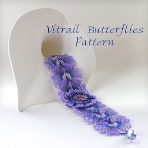 May include: A beaded bracelet in shades of purple and blue, featuring a floral design with a central embellishment. The bracelet is adorned with small beads and a dangling crystal. The text "Vitrail Butterflies Pattern" is visible.