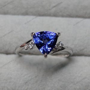 May include: A silver ring featuring a large, triangular, deep blue gemstone. The ring has a delicate band with small accent stones on either side of the main stone, creating a sophisticated and elegant design. A beautiful piece of jewelry.