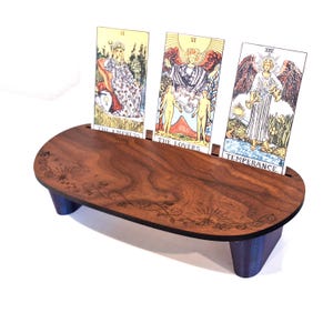 May include: A wooden tarot card holder with three cards displayed. The holder is dark brown with a decorative floral design. The cards feature illustrations and the titles "The Empress", "The Lovers", and "Temperance".