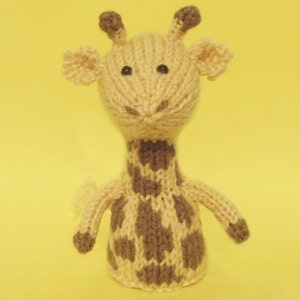 Può includere: Un giocattolo di giraffa di peluche lavorato a maglia con macchie marroni su uno sfondo crema. La girafa ha occhi neri e un naso marrone.