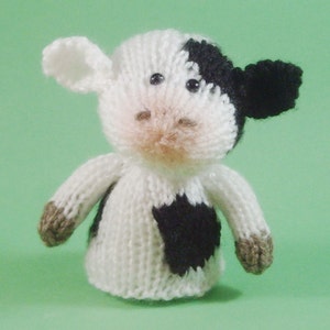 May include: A white and black knitted cow toy with brown accents. The cow has black eyes and a black spot on its side.