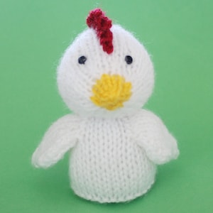 May include: A white knitted chicken toy with a red comb, yellow beak, and black eyes.