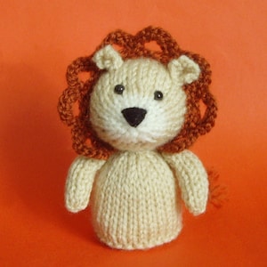 May include: A knitted lion toy with a white body and orange mane. The lion has black eyes and a black nose.