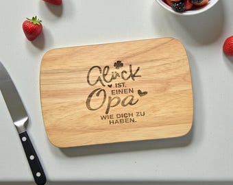 Könnte beinhalten: Rechteckiges Holzschneidebrett mit abgerundeten Ecken. Der deutsche Text "Glück ist, einen Opa wie dich zu haben" ist eingraviert. Erdbeeren, Brombeeren und ein Messer sind ebenfalls zu sehen.
