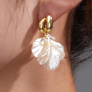 Peut inclure: Boucles d'oreilles créoles dorées avec un motif de fleur en perle blanche.