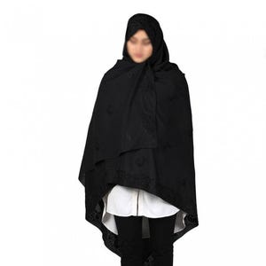 May include: A black shawl with intricate embroidery. The shawl is draped over a person's shoulders and head, with the edges of the shawl falling to the person's waist.