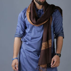 May include: A brown shawl with a gold patterned border. The shawl is worn over a blue shirt.