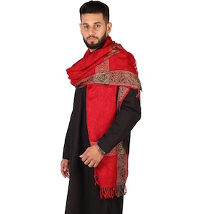 May include: A red shawl with gold and black trim. The shawl is draped around a person's neck and shoulders.