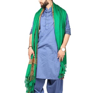 May include: A man wearing a blue long-sleeved shirt with a green shawl. The shawl has a gold and brown patterned border.