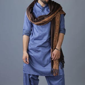 May include: A man wearing a blue long-sleeved shirt and matching pants with a brown and gold patterned shawl draped around his neck.