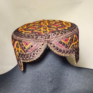 Może przedstawiać: Brązowa czapka z haftem, z żółtymi i czerwonymi szwami. Czapka ma falbankę i tradycyjny wzór.