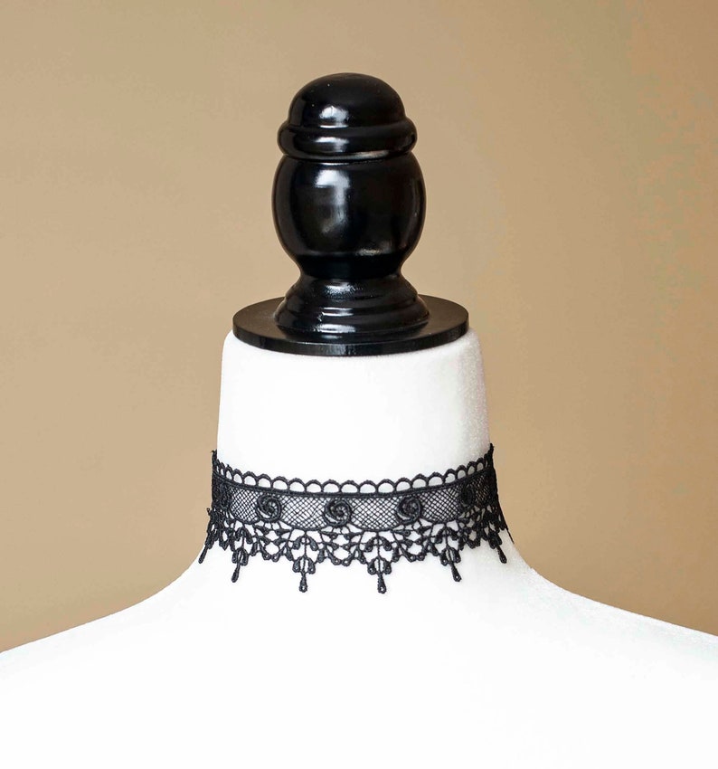 May include: A black lace choker necklace with a delicate floral design. The choker is displayed on a white mannequin bust.